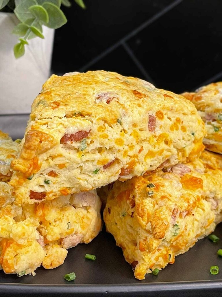 Ham and cheese scones stacked on a dark platter garnished with chopped chives.