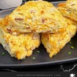 Ham and cheese scones stacked on a dark plate garnished with chopped chives.
