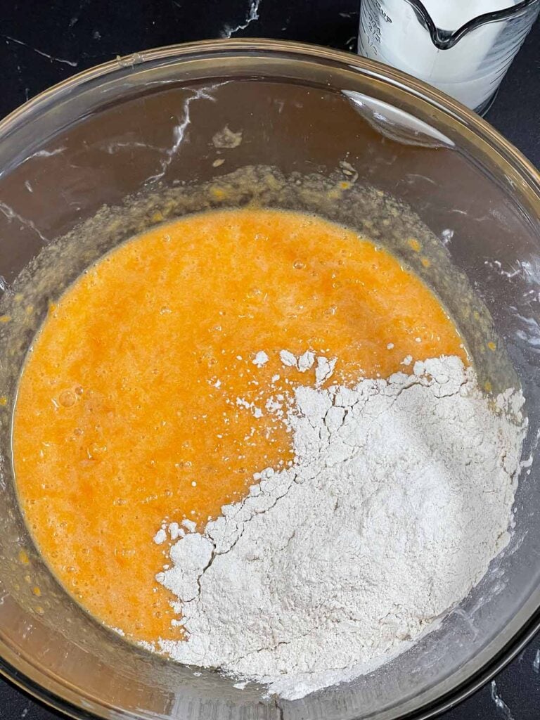 Half of the dry ingredients added to the wet ingredients in a glass bowl.