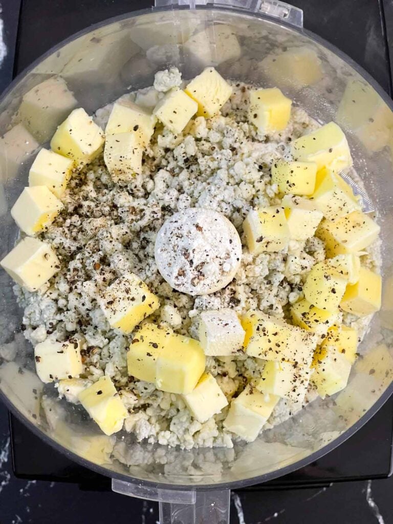 Flour, cubed butter, crumbled blue cheese, and cracked black pepper in the bowl of a food processor.