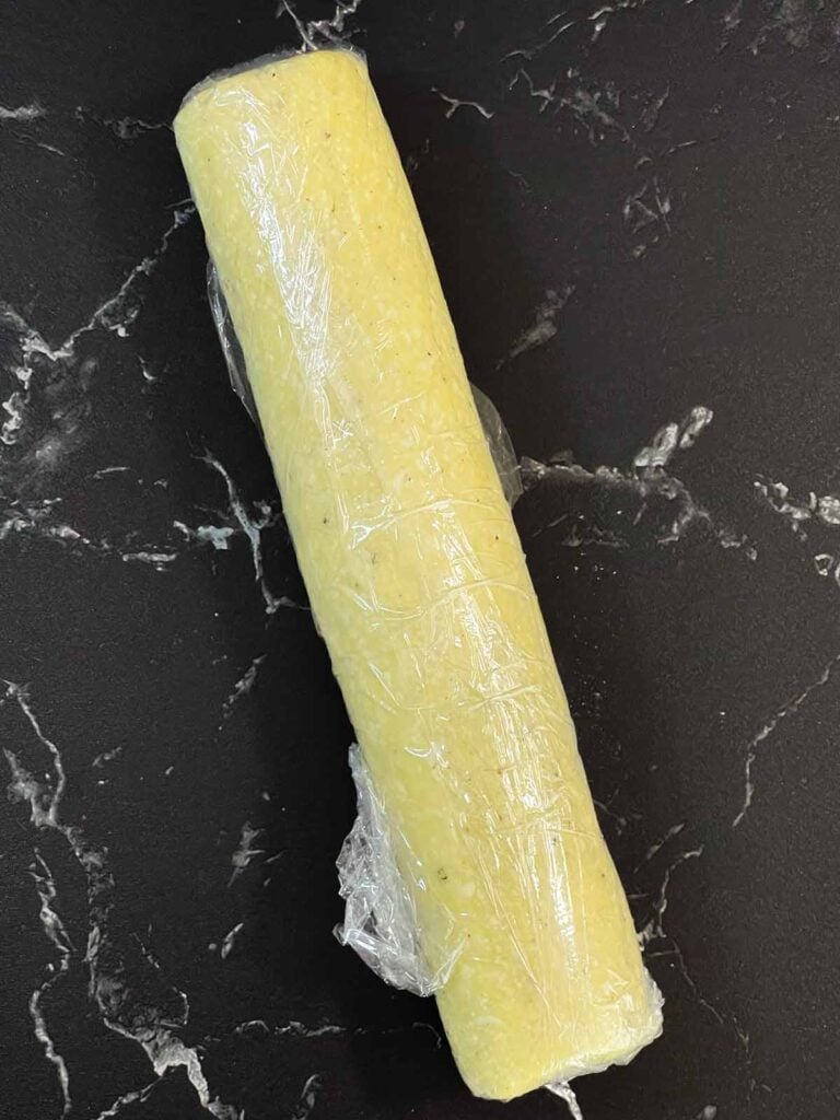 Blue cheese wafer dough log wrapped in plastic wrap on a dark surface.