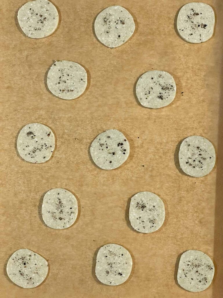 Raw blue cheese wafers on a parchment paper lined baking sheet.