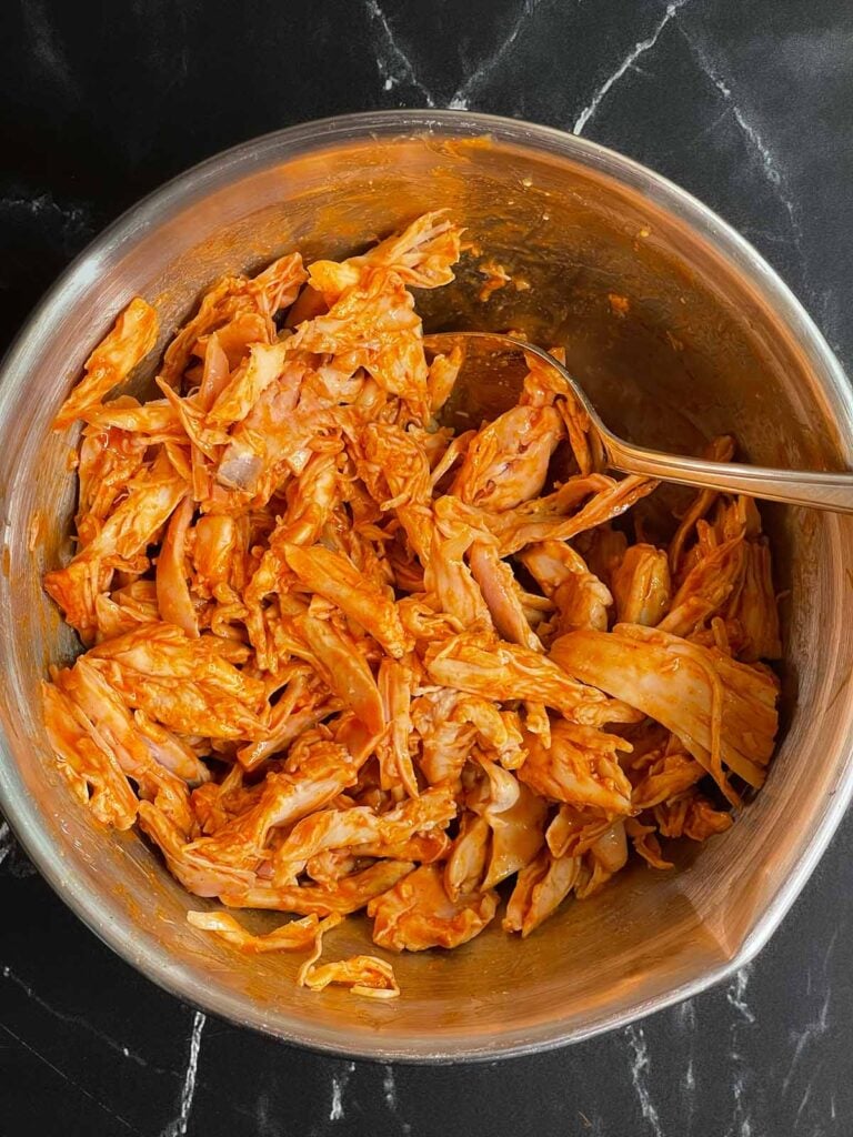 Buffalo chicken shredded in a stainless steel bowl.