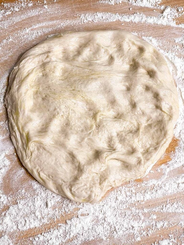 Pizza dough on a cutting board with flour about.