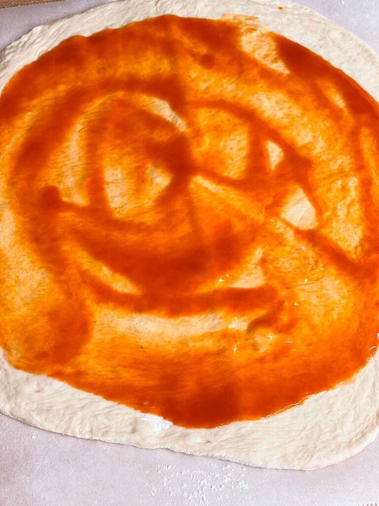 Pizza dough with buffalo sauce on it.