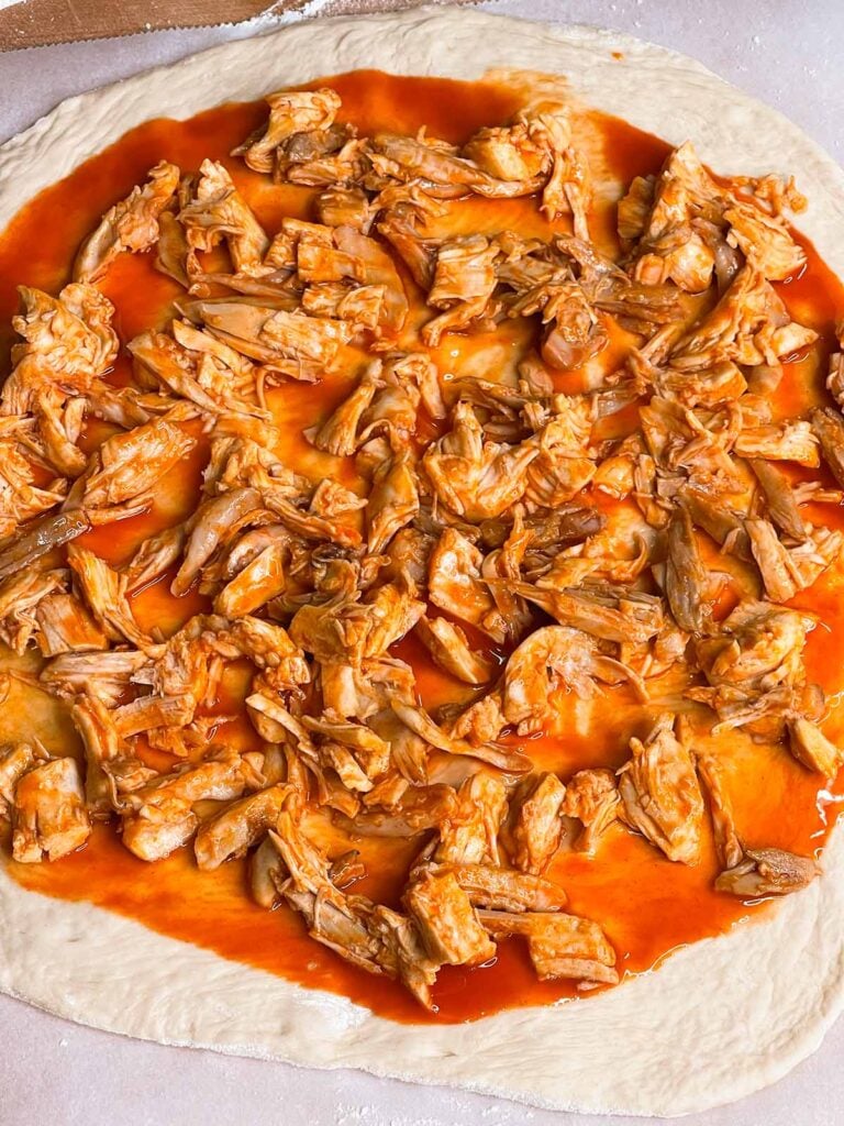 Buffalo chicken pizza being assembled.