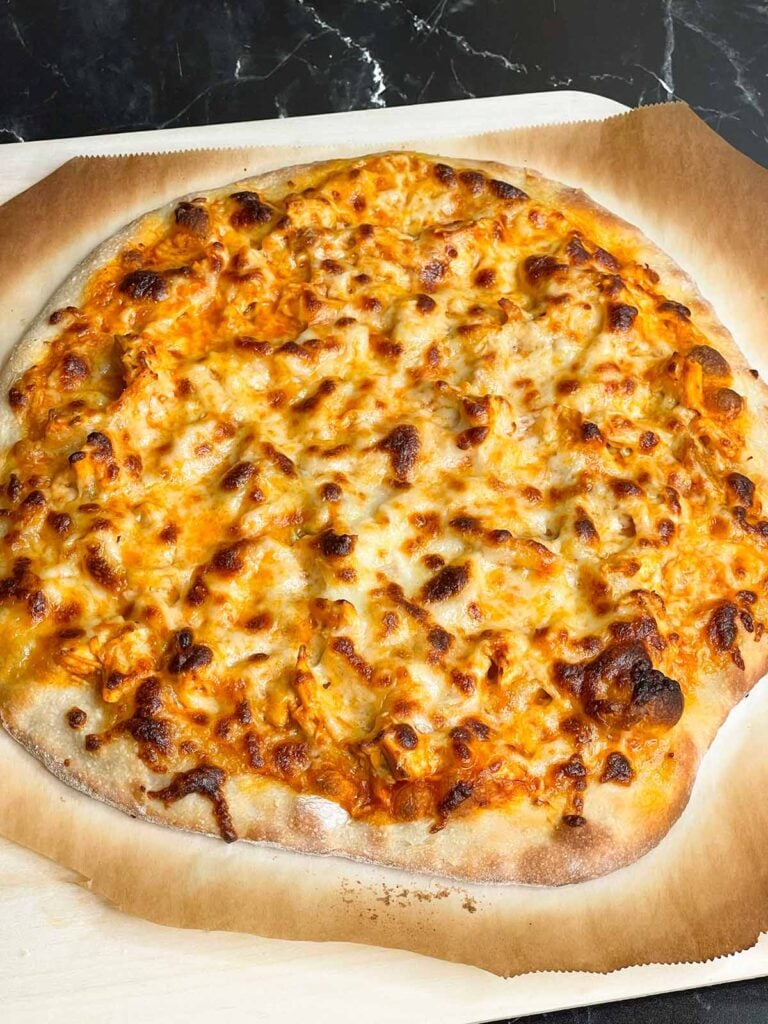 A buffalo chicken pizza on a cutting board right out of the oven.