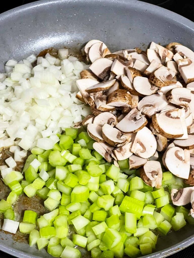 Mixed raw vegetables and mushrooms in a skilket.
