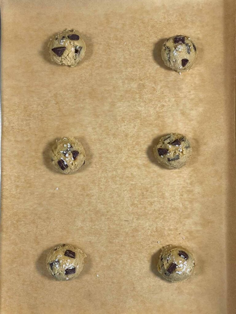 Chocolate chip cookie dough balls on a parchment paper lined baking sheet.