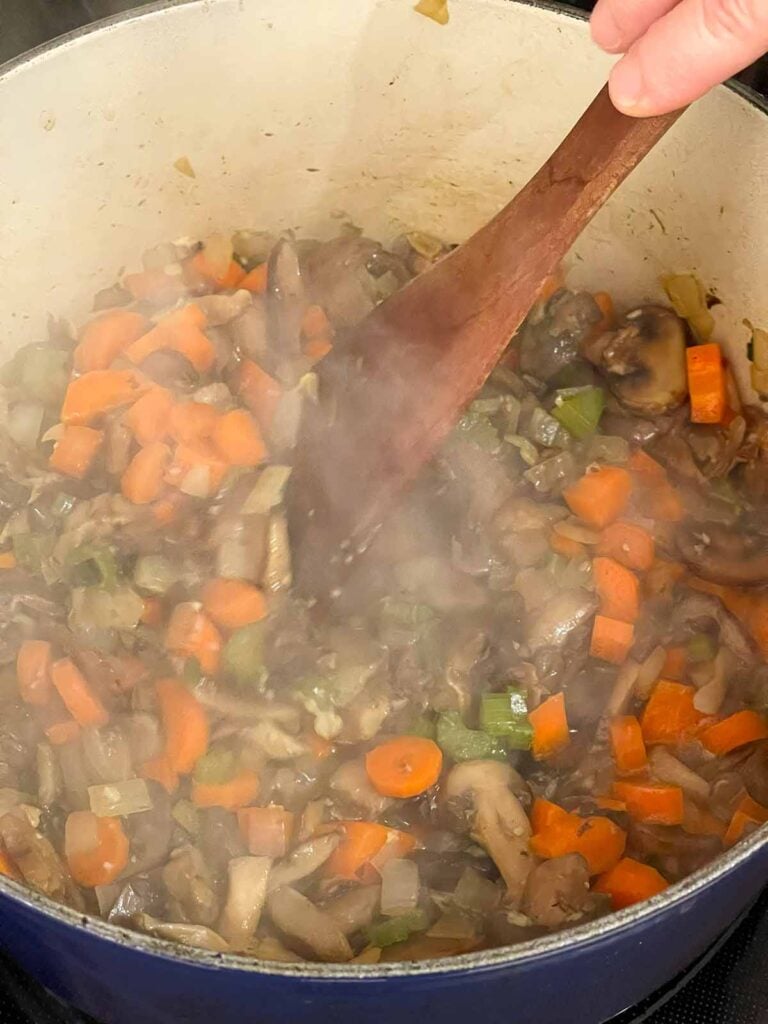 Stirring the vegetables cooking the a Dutch oven for mushroom barley soup.