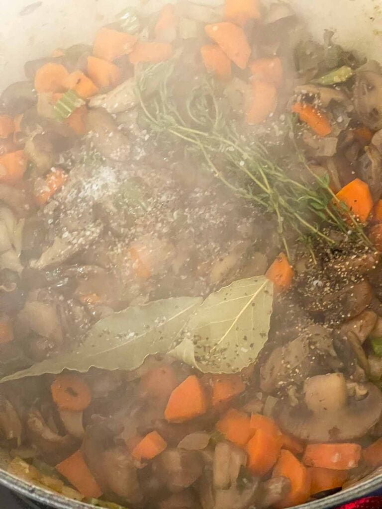 Bay leaves, fresh thyme, kosher salt, and black pepper added to the vegetables.