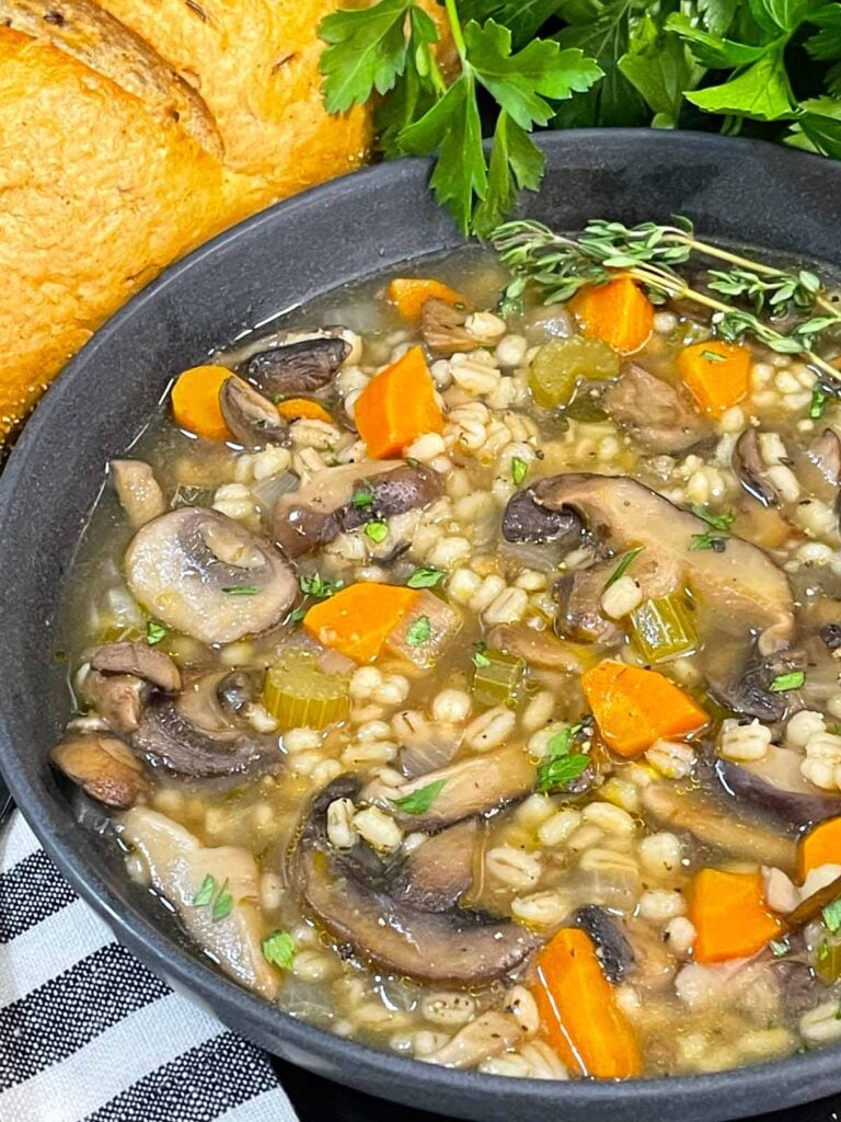 Mushroom barley soup in a dark bowl garnished with minced parsley and fresh thyme.
