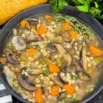 Mushroom barley soup in a dark bowl garnished with minced parsley and fresh thyme.