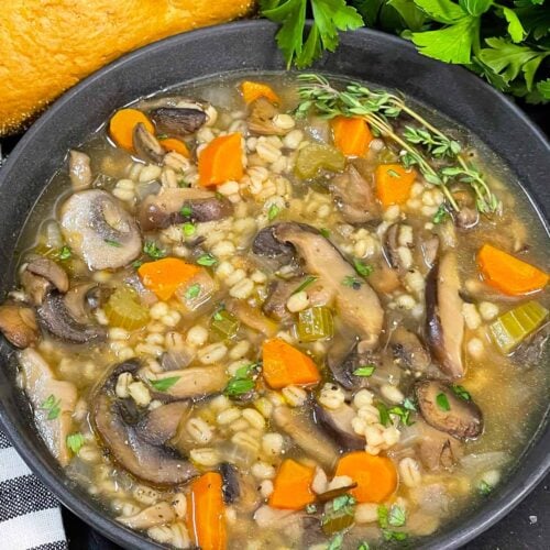 Mushroom barley soup in a dark bowl garnished with minced parsley and fresh thyme.