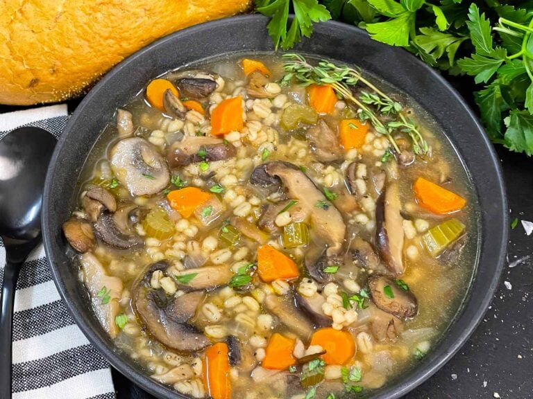 Mushroom barley soup in a dark bowl garnished with minced parsley and fresh thyme.