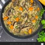 Mushroom barley soup in a dark bowl garnished with minced parsley and fresh thyme.