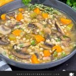 Mushroom barley soup in a dark bowl garnished with minced parsley and fresh thyme.