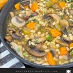 Mushroom barley soup in a dark bowl garnished with minced parsley and fresh thyme.
