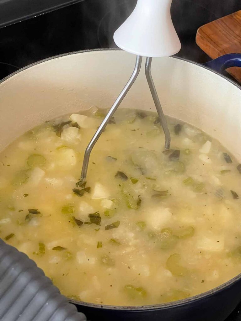 Potato masher mashing some of the potatoes in the soup.