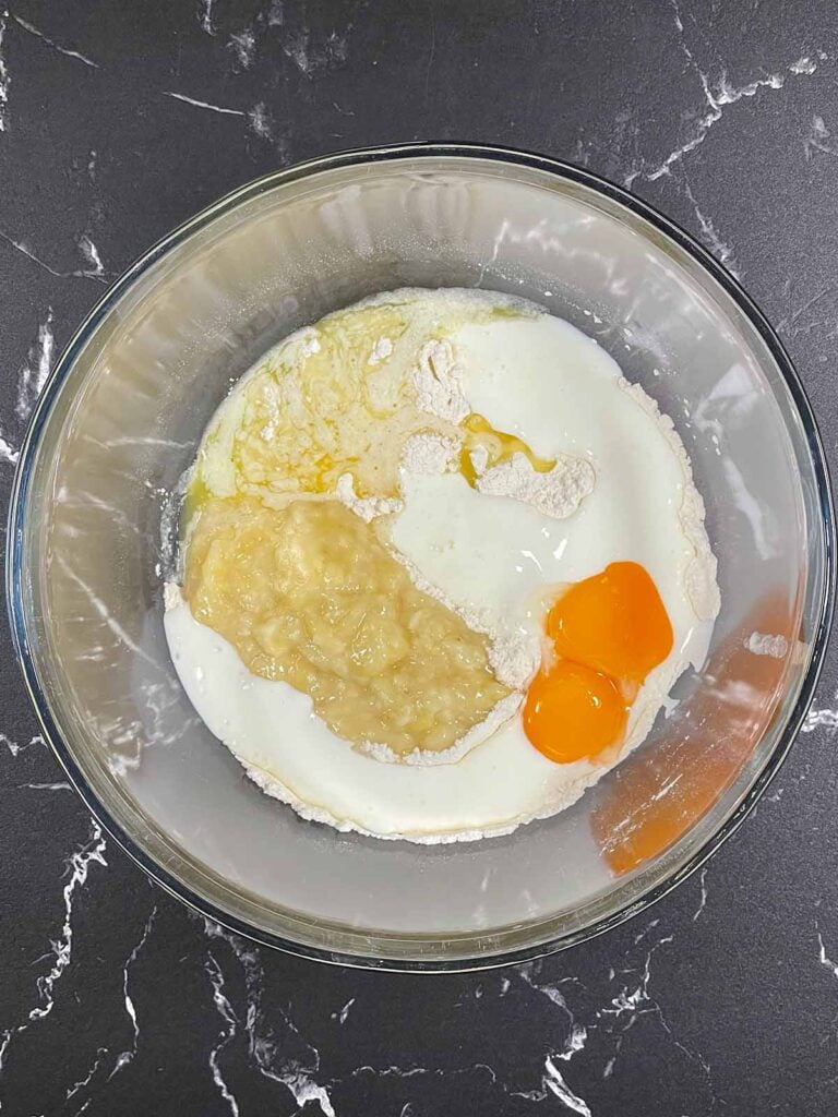 Banana pancake batter with buttermilk, egg yolks, and melted butter in the mixing bowl with the dry ingredients.