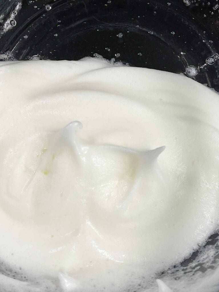 Egg whites beaten to stiff peaks in a glass mixing bowl.