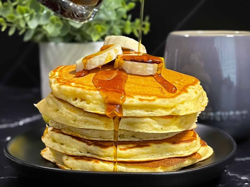 Fluffy banana pancakes stacked high with golden edges and soft centers, served with syrup and sliced bananas.