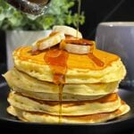 Fluffy banana pancakes stacked high with golden edges and soft centers, served with syrup and sliced bananas.