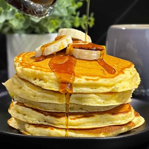 Fluffy banana pancakes stacked high with golden edges and soft centers, served with syrup and sliced bananas.