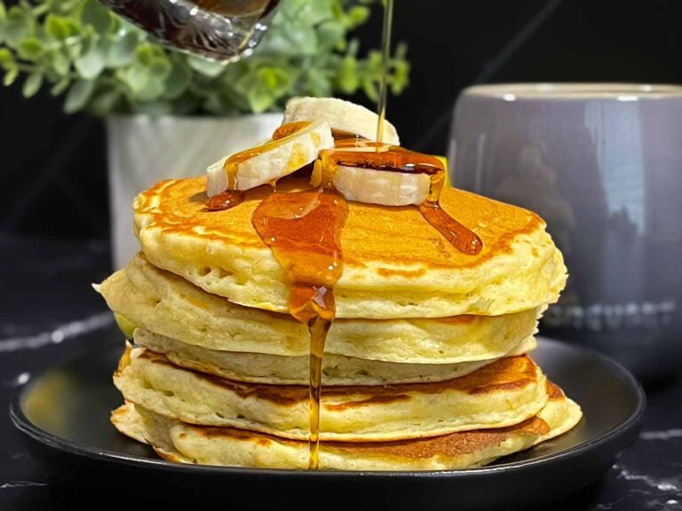 Fluffy banana pancakes stacked high with golden edges and soft centers, served with syrup and sliced bananas.