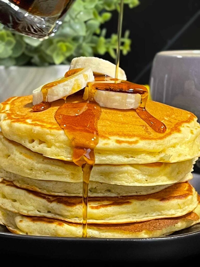 Fluffy banana pancakes stacked high with golden edges and soft centers, drizzled with maple syrup.