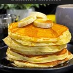 Fluffy banana pancakes stacked high with golden edges and soft centers, served with syrup and sliced bananas.