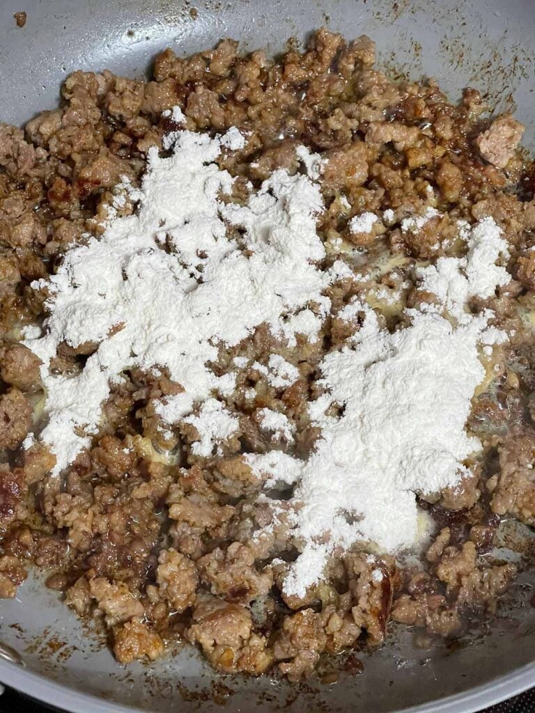 Flour added to sausage in a skillet.