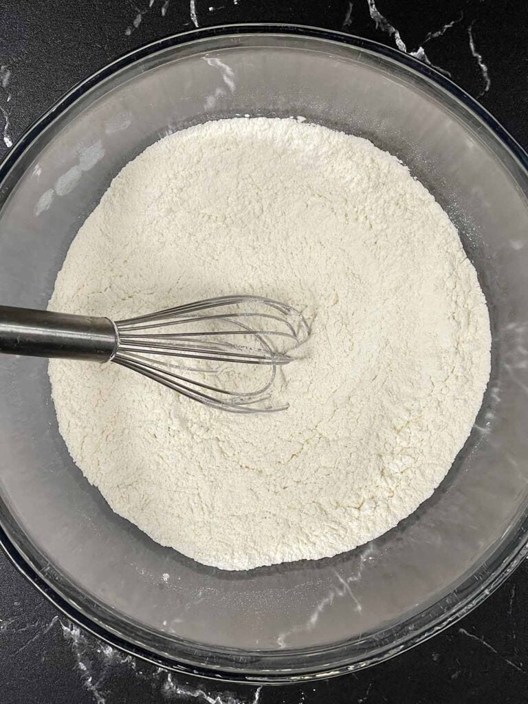 Dry ingredients for biscuits whisked together in a glass bowl.