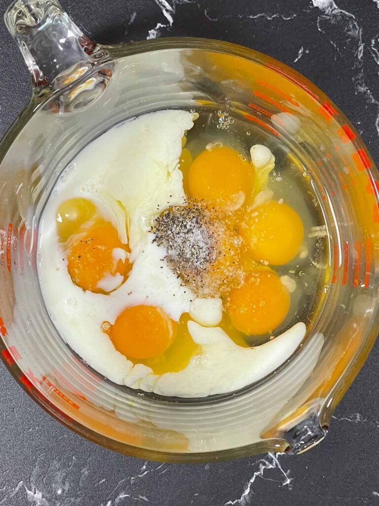 Eggs, milk, salt and pepper together in a glass bowl.