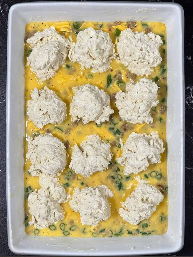 Raw drop biscuits added to 9x13 baking dish with sausage egg mixture on the bottom.