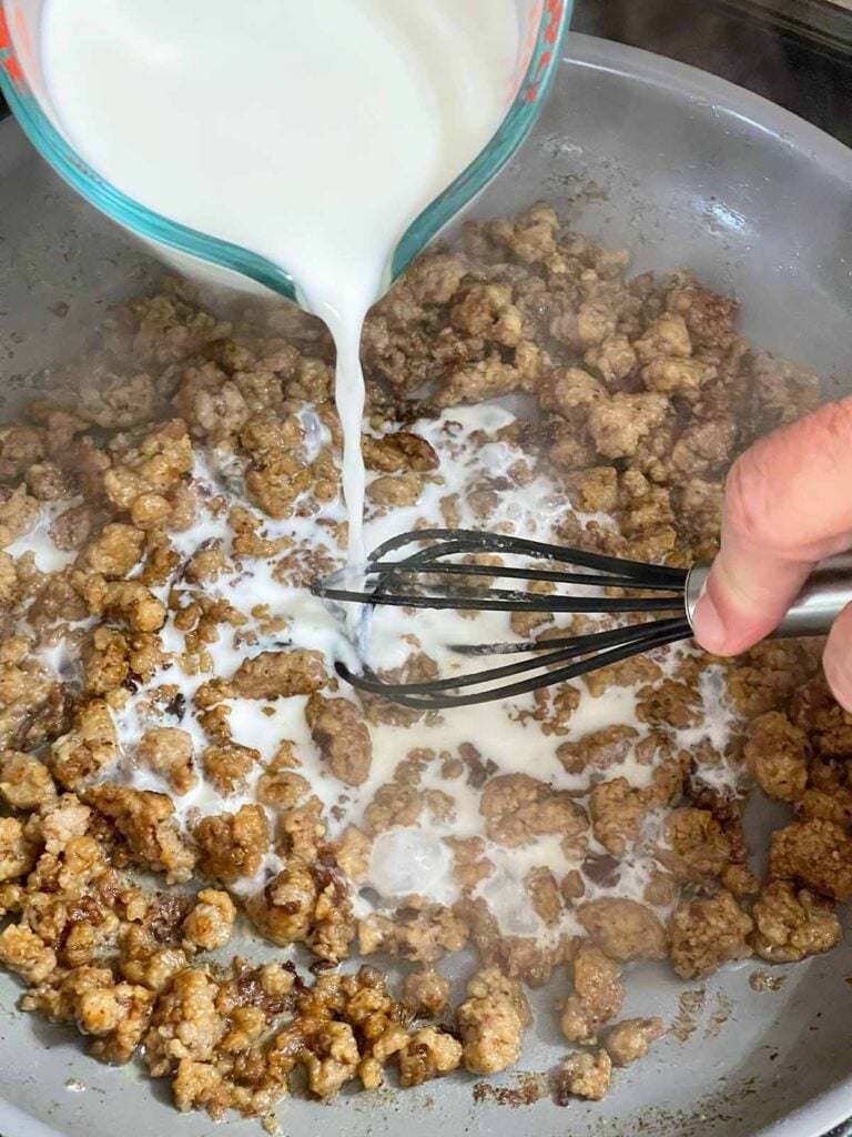 Whisking milk into the beginnings of sausage gravy.