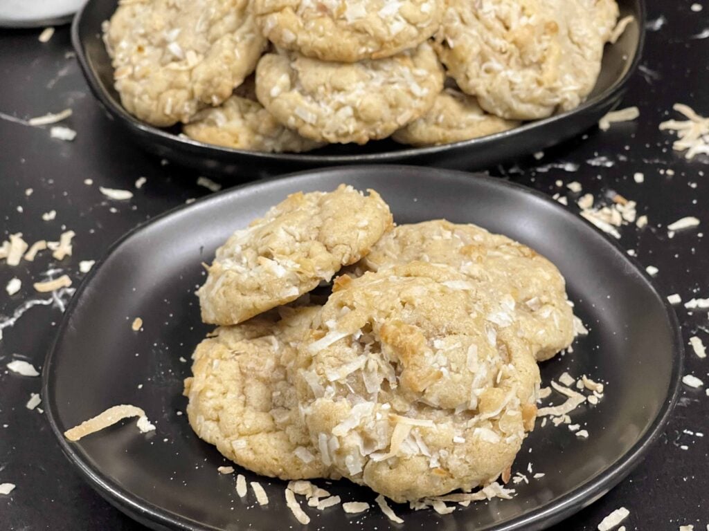 Stack of chewy coconut cookies on a dark plate sprinkled with toasted shredded coconut.