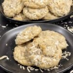 Stack of chewy coconut cookies on a dark plate sprinkled with toasted shredded coconut.