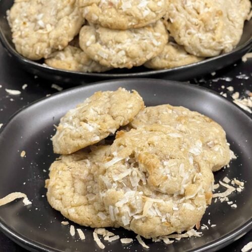 Stack of chewy coconut cookies on a dark plate sprinkled with toasted shredded coconut.