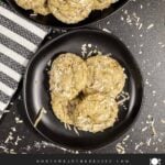 Stack of chewy coconut cookies on a dark plate sprinkled with toasted shredded coconut.