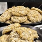 Stack of chewy coconut cookies on a dark plate sprinkled with toasted shredded coconut.