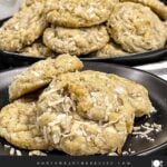 Stack of chewy coconut cookies on a dark plate sprinkled with toasted shredded coconut.