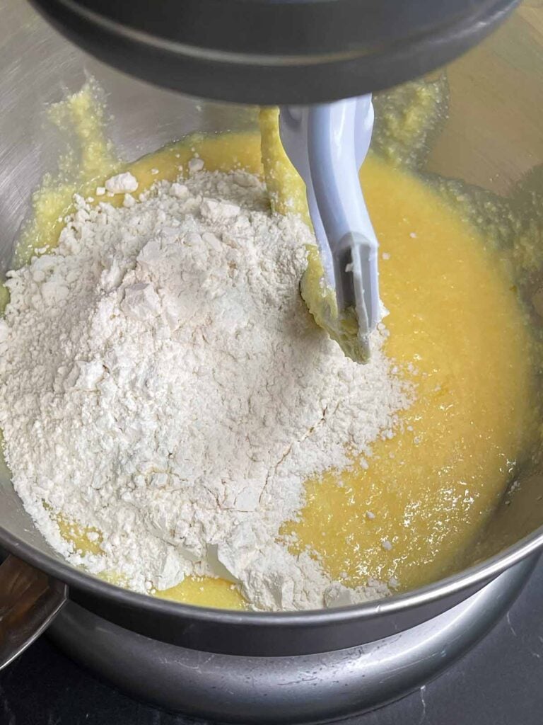 Dry ingredients being added to the wet ingredients in a metal mixing bowl.