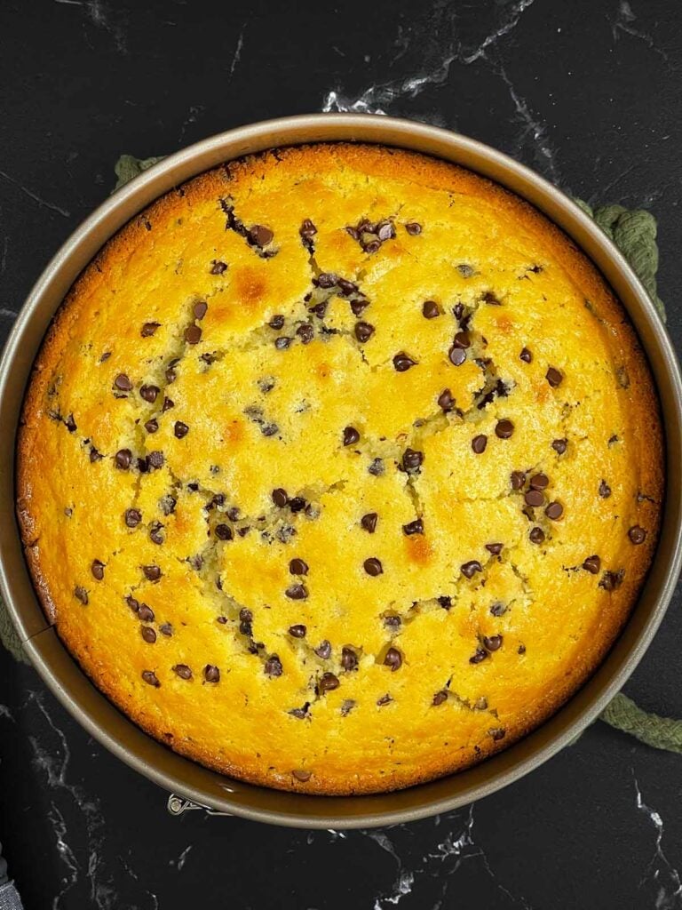 Baked chocolate chip ricotta cake in a metal springform pan on a dark surface.