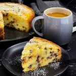 A slice of chocolate chip ricotta cake garnished with powdered sugar on a dark plate.