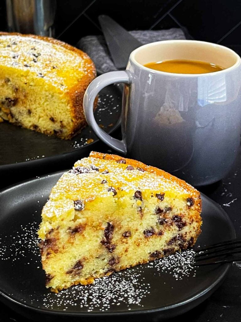 A slice of chocolate chip ricotta cake garnished with powdered sugar on a dark plate.
