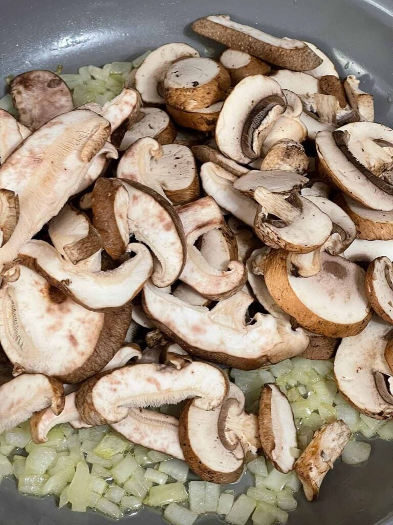 Mushrooms just added to a skillet with cooked onions.