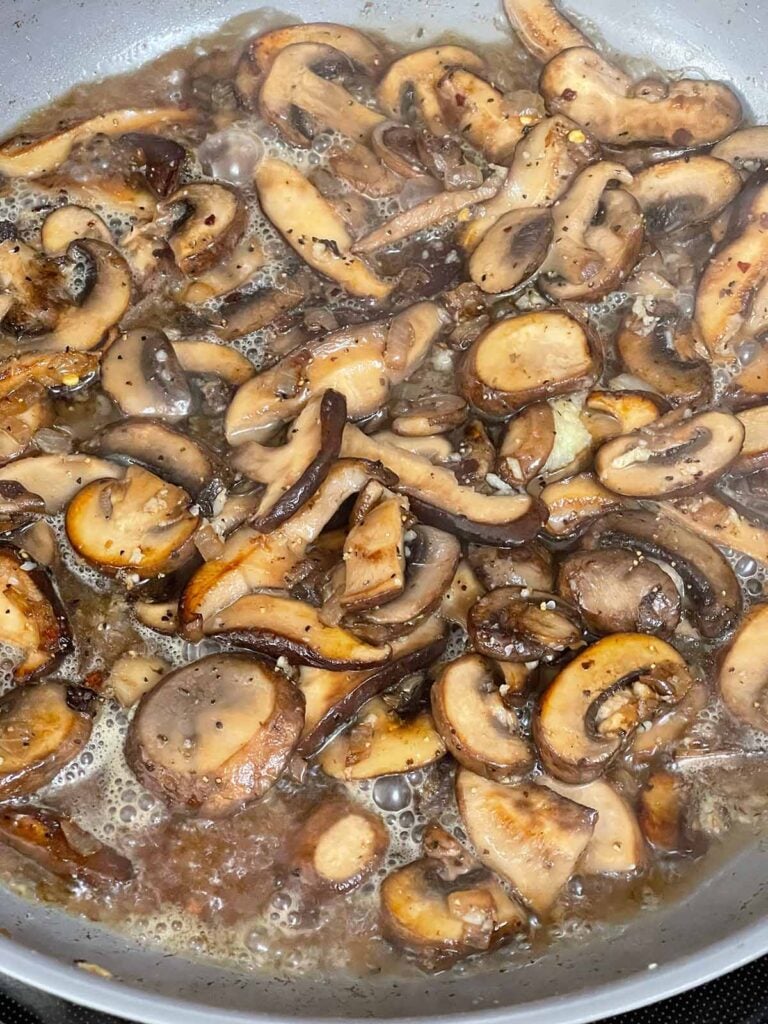 Wine and mushrooms cooking in a skillet.