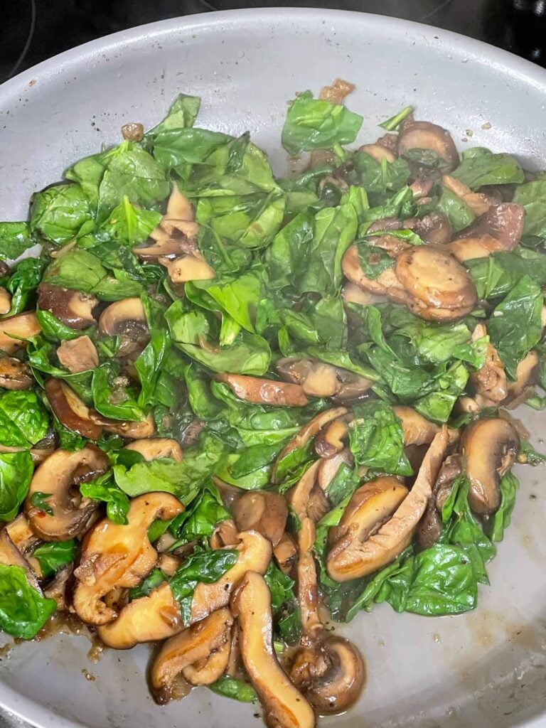 Spinach and mushrooms in a skillet cooking.