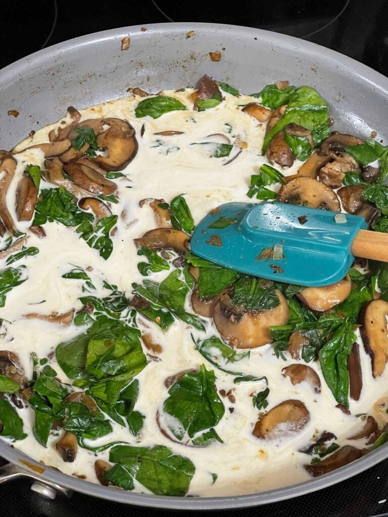 Building a cream sauce in a skillet with mushrooms and spinach.